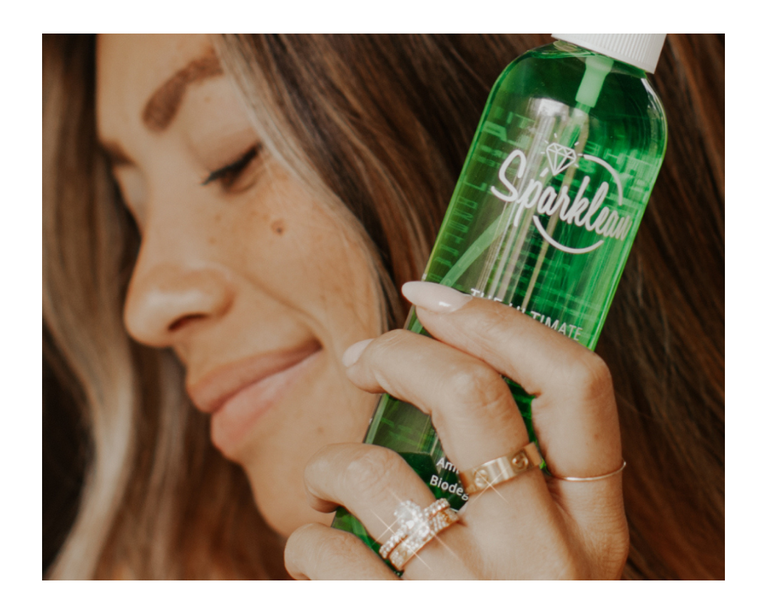 Woman holding a green spray bottle labeled 'Sparklean' with a blurred background